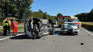 Nach einem Unfall auf einer Autobahn liegt ein schwerbeschädigtes Auto auf der Seite. 