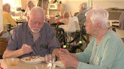 Zwei Senioren sitzen in einem Pflegeheim am Tisch und essen.