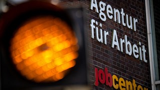 Eine Ampel leuchtet vor der Agentur für Arbeit und dem Jobcenter.