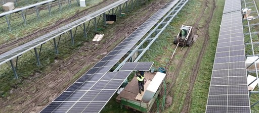 Arbeiter mit Landmaschinen setzen Solarzellen auf Metallgerüst