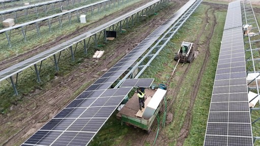 Arbeiter mit Landmaschinen setzen Solarzellen auf Metallgerüst