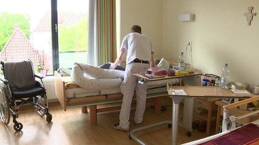 Eine Person wird von einem Pfleger im Krankenbett versorgt.