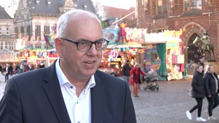 Ein Mann, Andreas Bovenschulte steht vor der Kamera - Im Hintergrund sind blinkende Lichter zu sehen