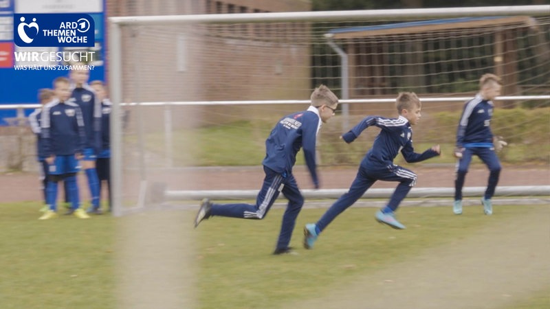 Zwei Jungen in Sportklamotten des Leher TS rennen über einen Fußballplatz.