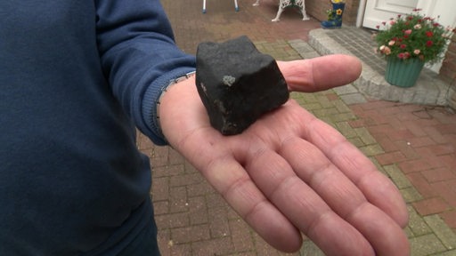 Ein Mann hält einen schwarzen Brocken, genauer einen Asteroiden in der Hand.