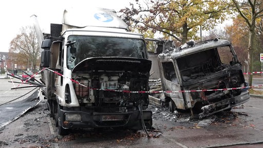 Zwei ausgebrannte LKW´s stehen nebeneinander auf einem Parkplatz.