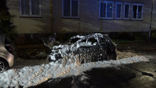 Ein abgebranntes Auto mit Löschschaum besprüht