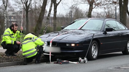 Zu sehen ist ein verunfalltes Auto, welches von Polizeibeamten gesichert wird.