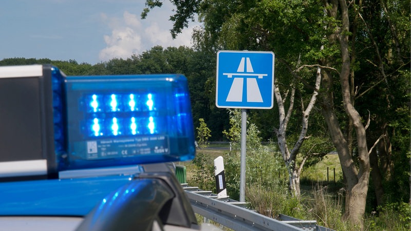 Ein Polizeiauto mit Blaulicht steht vor einem Autobahnschild.