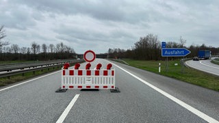 Auf einer leeren Autobahn steht neben einer Ausfahrt eine Absperrung.