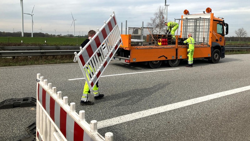 Bauarbeiter räumen eine Absperrung auf einer Straße weg.