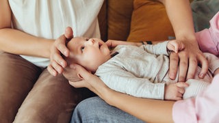 Ein Baby liegt auf den Knien der Mutter, während eine zweite Frau dem Baby den Bauch massiert.