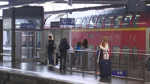 Personen warten am Gleis auf ihre Bahn.