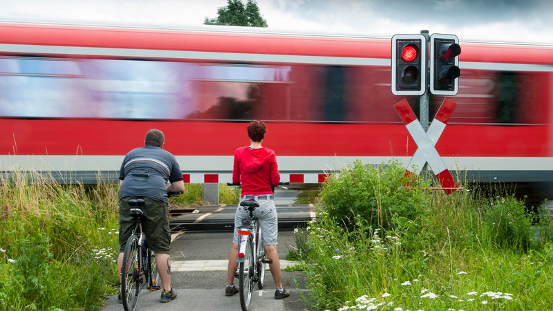 Mann und Frau stehen mit Fahrrädern an einem geschlossenen Bahnübergang