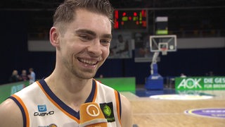 Basketball-Profi Adrian Breitlauch von den Eisbären Bremerhaven strahlt nach dem Sieg gegen Bayreuth bei einem Interview.