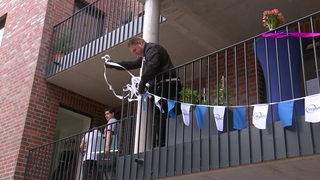 Ein Mann hängt Fahnen auf einem Balkon auf