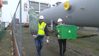 Mitarbeiter der Seemannsmission tragen einen Weihnachtsbaum und Geschenke