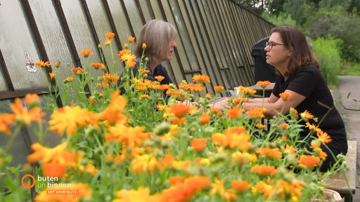 Swei Frauen sitzen an einem Tisch, davor Blumen