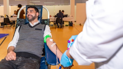 Ein Mann auf einem bequemen Stuhl sitzend beim Blutspenden in einem Zentrum neben einer Krankenschwester in Uniform. 