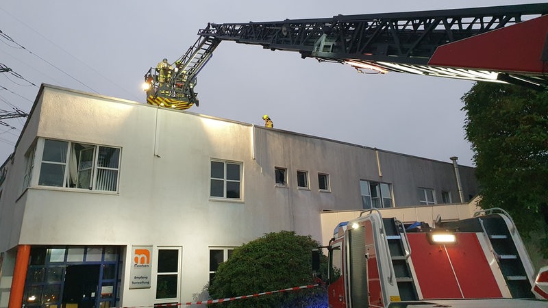 Feuerwehrleute löschen ein Gebäudedach von einer Drehleiter aus.