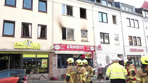 Vor einem Wohnhaus auf einer Straße stehen mehrere Feuerwehrmänner.