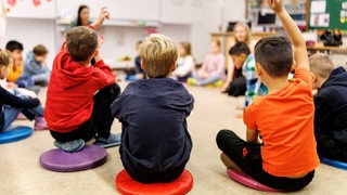 Schüler einer Grundschulklasse sitzen während des Unterrichts in einem Kreis auf dem Boden des Klassenzimmers zusammen und melden sich.