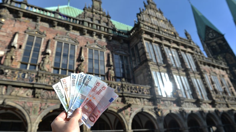 Hinter einem Geldscheinfächer ist das Rathaus von Bremen zu sehen. 