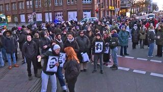 Zahlreiche Menschen stehen in Bremen auf einer Kreuzung und halten Bilder der Toten vom Anschlag in Hanau hoch.