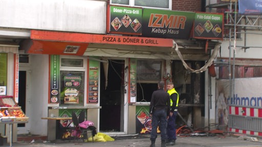Vor einem ausgebrannten Döner-Imbiss in der Bremer Neustadt stehen zwei Polizisten.