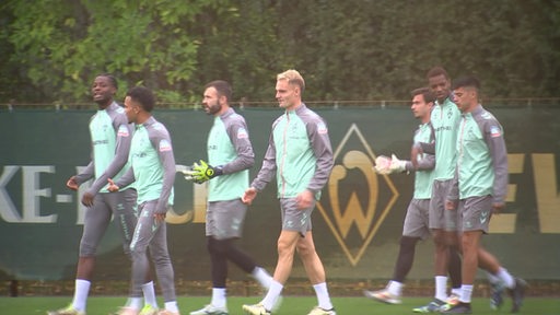 Mehrere Mannschaftsmitglieder von Werder Bremen betreten in Trikots ihren Trainingsplatz