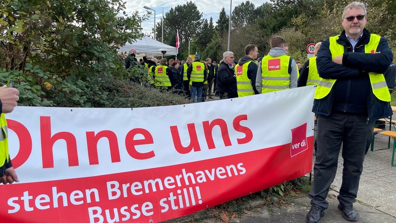 Mehrere Menschen mit Warnwesten stehen neben einem Plakat.