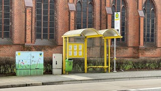 Eine menschenleere Bushaltestelle steht vor einer Kirche.