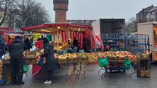 Auf einem Platz zwischen Gebäuden stehen Marktstände und vereinzelt Personen.