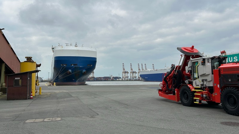 Ein blau-weißes Schiff liegt an einem Kai in einem Hafengebiet.