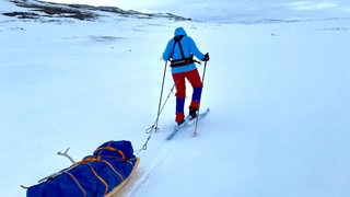 Eine junge Frau fährt mit einem Schlitten auf Skiern durch die Eiswüste 