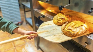 Ein Bäcker holt frisches Brot aus dem Ofen
