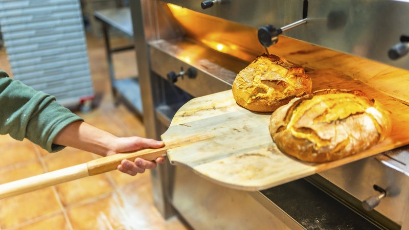 Ein Bäcker holt frisches Brot aus dem Ofen