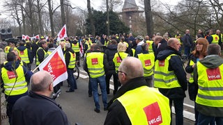 Menschen mit gelben Warnwesten stehen in der Bremer Innenstadt, im Hintergrund die Windmühle am Wall.