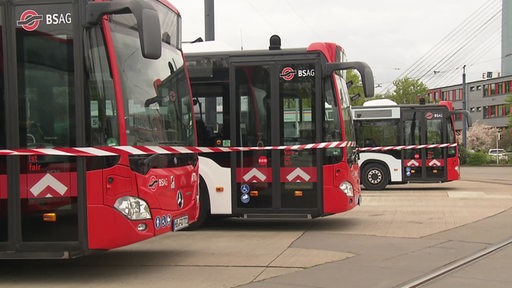 Drei Busse der BSAG sind auf einem Parkplatz, hinter einem Absperrband zu sehen.