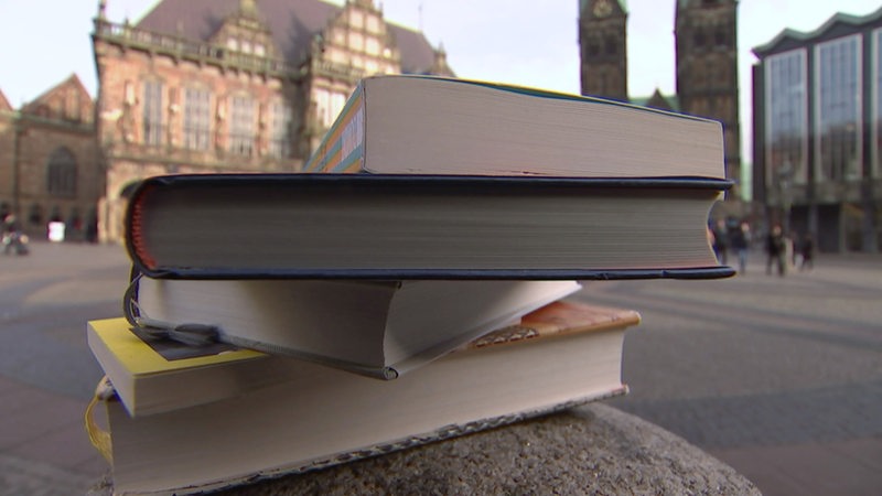 Im Vordergrund sind Bücher gestapelt, im Hintergrund der Bremer Marktplatz zu sehen.