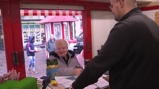 Malte Oldenburger steht in seinem Tombolastand und verkauft Lose an eine Frau.