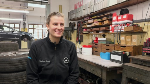 Eine junge KFZ-Mechatronikerin sitzt in einer Autowerkstatt.