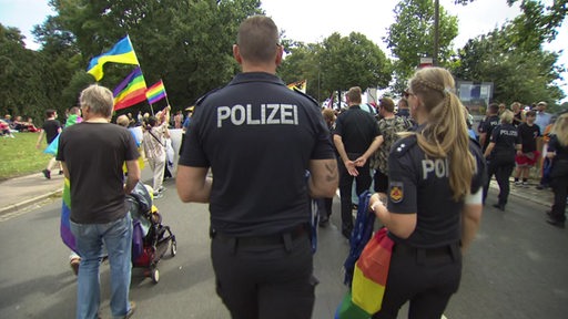 Zwei Polizistinnen und Polizisten bem CSD-Demozug mit Regenbogenflagge.