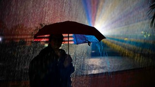 Eine Person steht im Dunkeln mit einem Regenschirm im Regen.