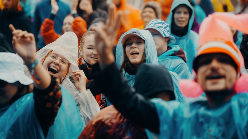 Mit Regenponchos ausgestattete Menschen feiern auf dem Deichbrand-Festival und trotzen dem schlechten Wetter.