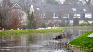 Sandsäcke liegen auf einem Deich vor evakuierten Wohnhäusern an der Wörpe in Lilienthal.