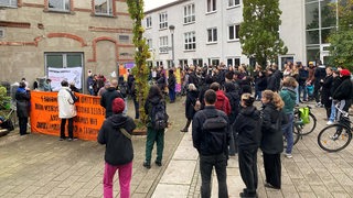 Mehrere Dutzend Menschen stehen bei einer Demonstration in einem Halbkreis.