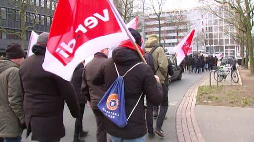 Demonstrierende mit Fahnen von Verdi laufen gemeinsam durch die Stadt