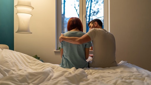 Ein Mann sitzt tröstend neben einer Frau auf dem Bett (Symbolbild)