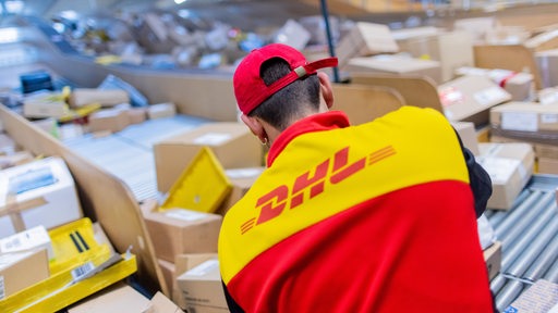 Ein Paketzusteller sortiert und räumt in einer Zustellbasis von Deutsche Post DHL Pakete in ein Zustellfahrzeug.